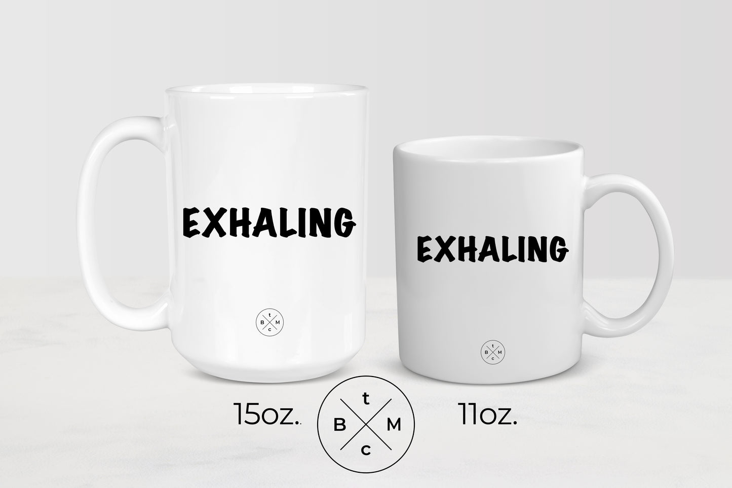 White 11 ounce and 15 ounce ceramic mugs with black text exhaling