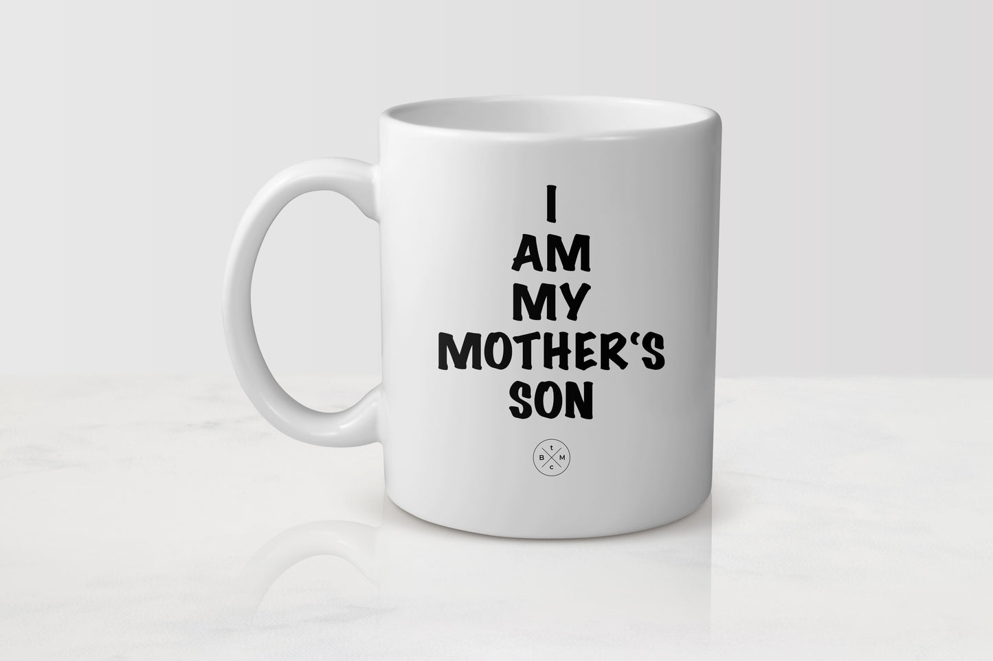 11 ounce white ceramic mug with black text I am my mother’s son