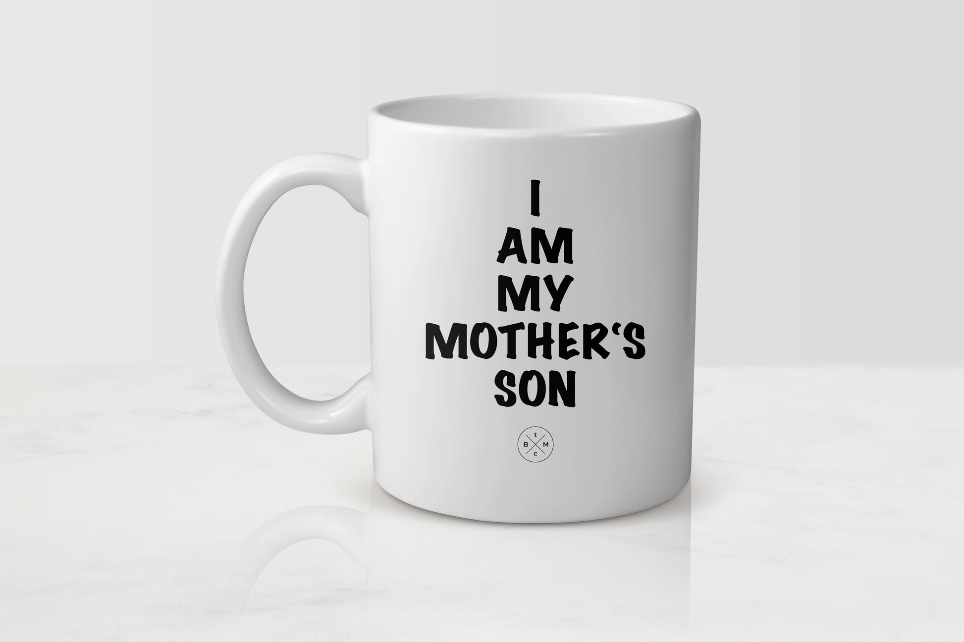 11 ounce white ceramic mug with black text I am my mother’s son