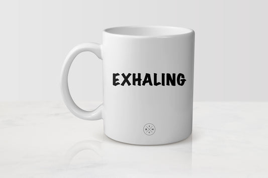 White 11 ounce ceramic mug with black text exhaling