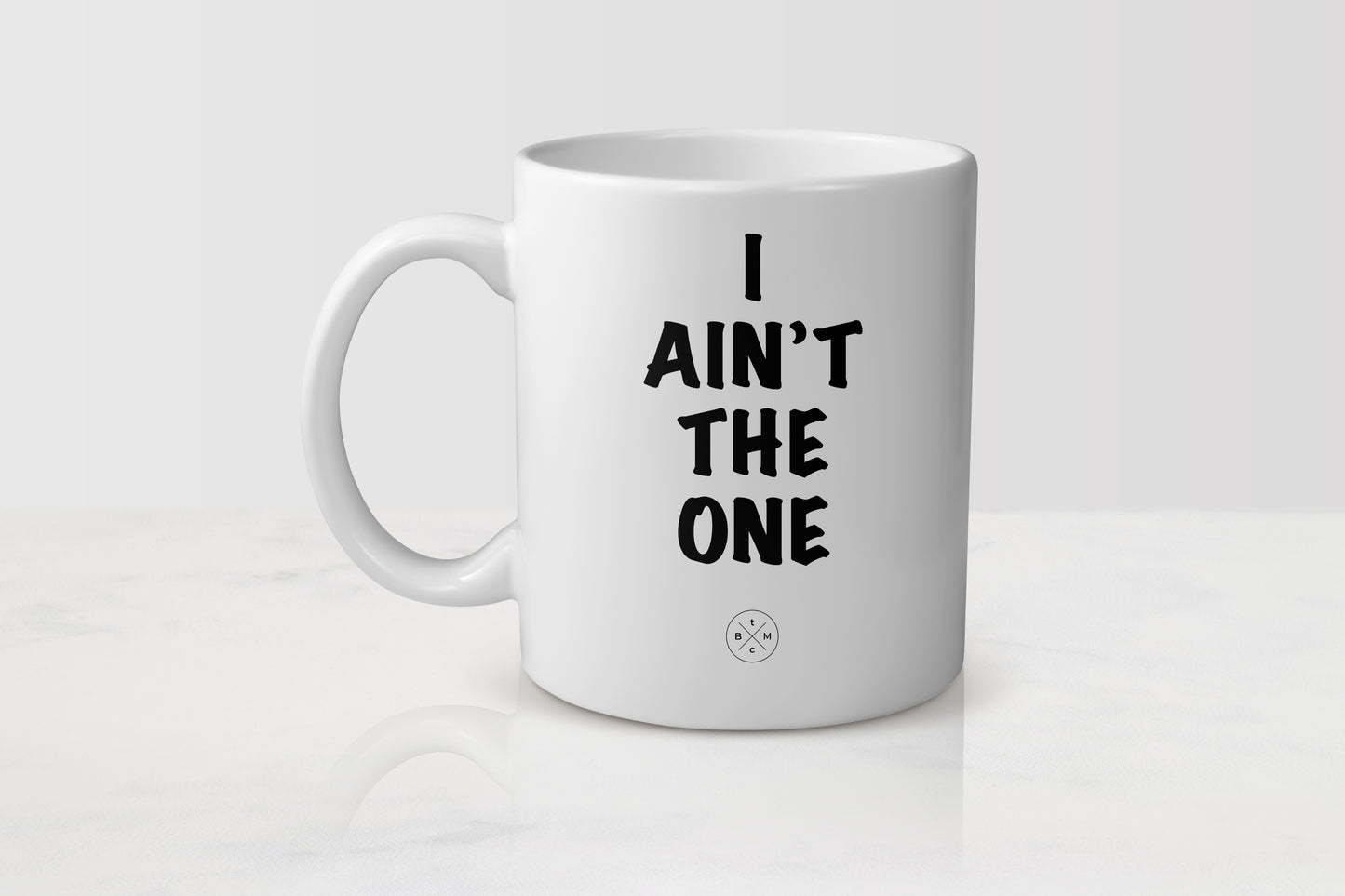 11 ounce white ceramic mug with black text I ain’t the one