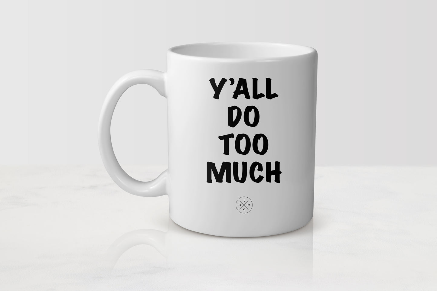 White 11 ounce ceramic mug with black text y’all do too much