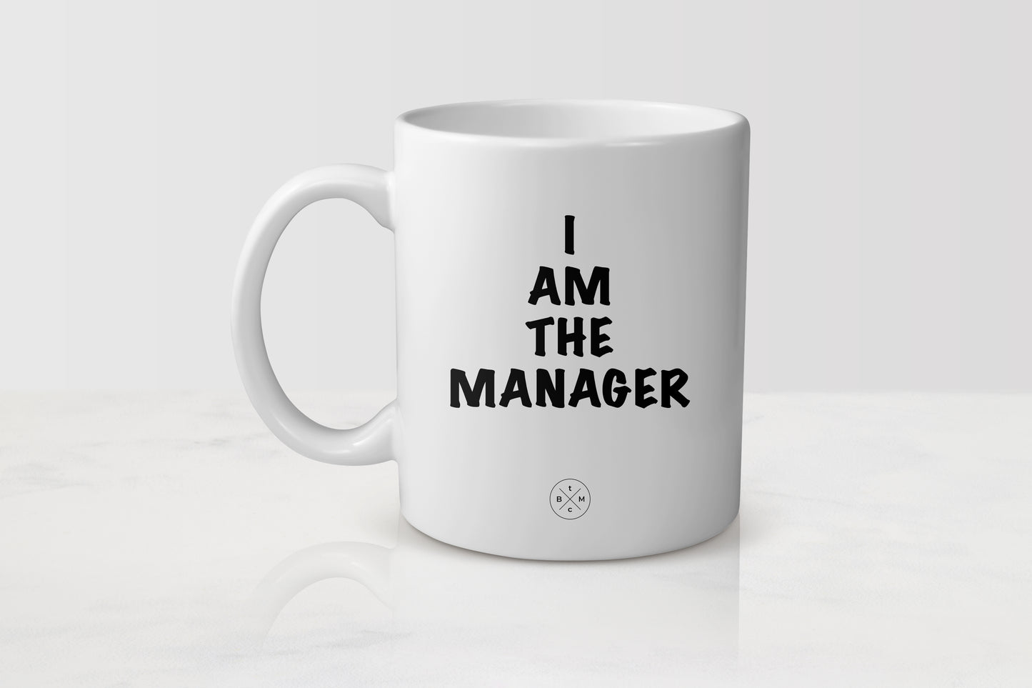 11 ounce white ceramic mug with black text I am the manager