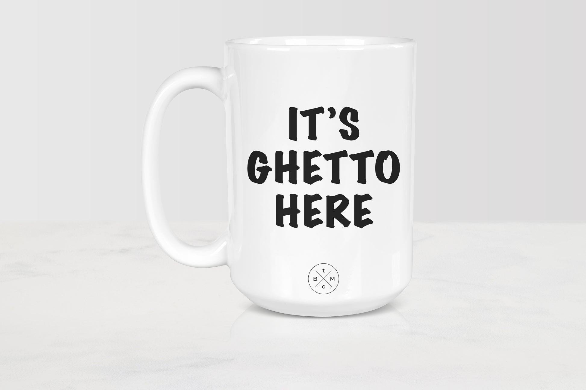 White 15 ounce ceramic mug with black text it’s ghetto here 