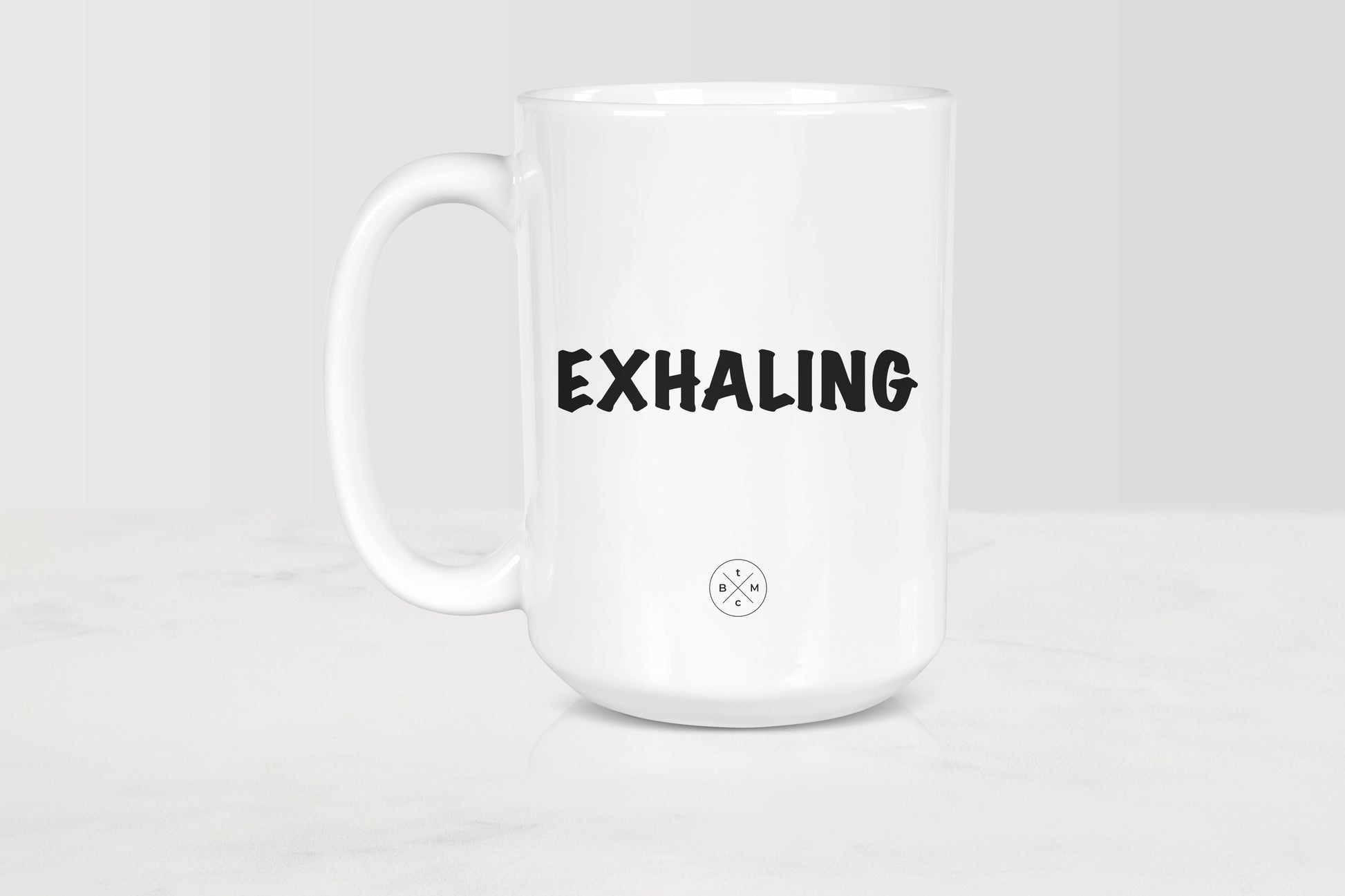 White 15 ounce ceramic mug with black text exhaling