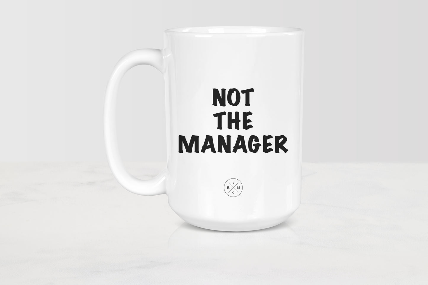 15 ounce white ceramic mug with black text not the manager