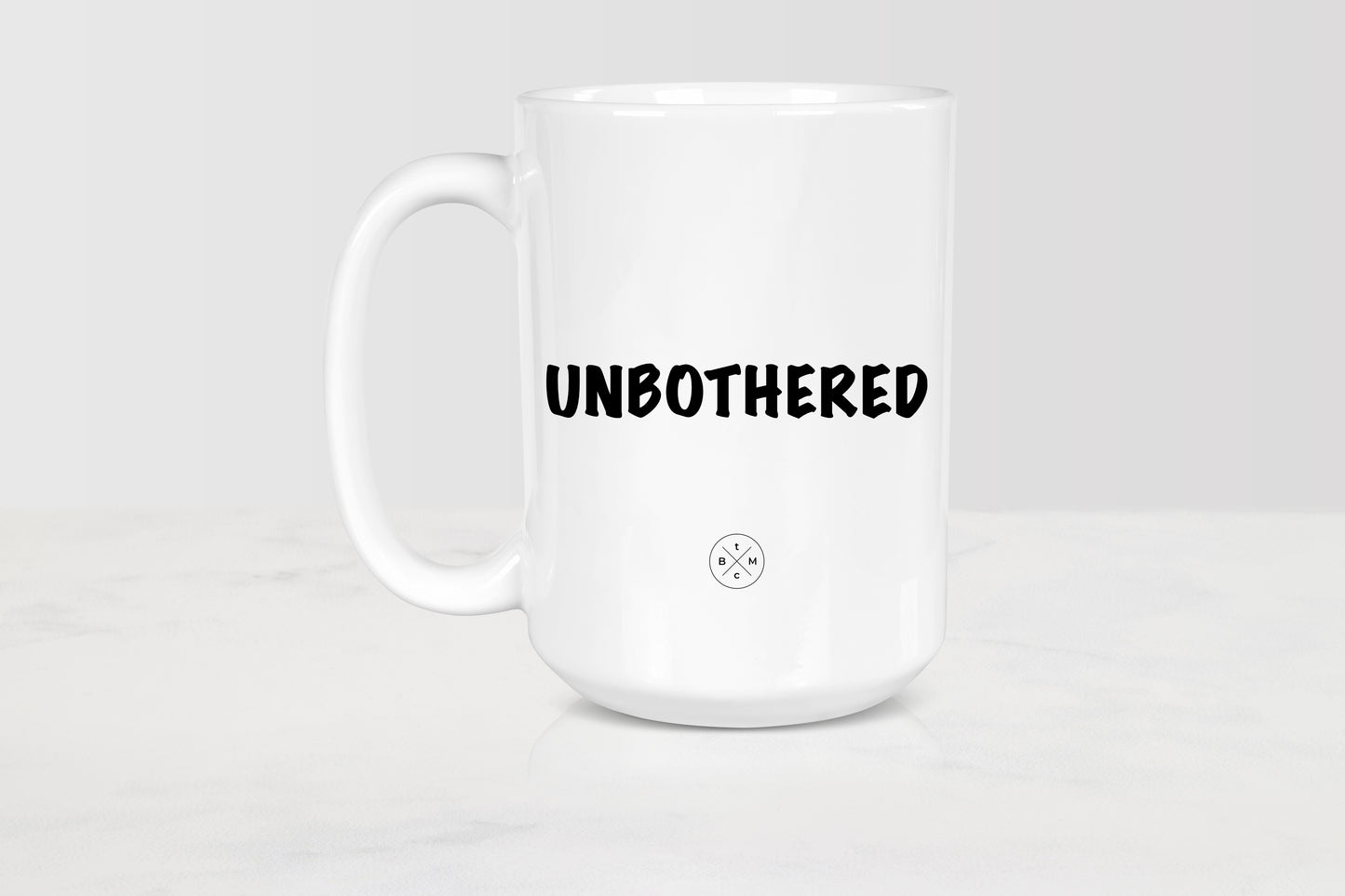 White 15 ounce ceramic mug with black text unbothered