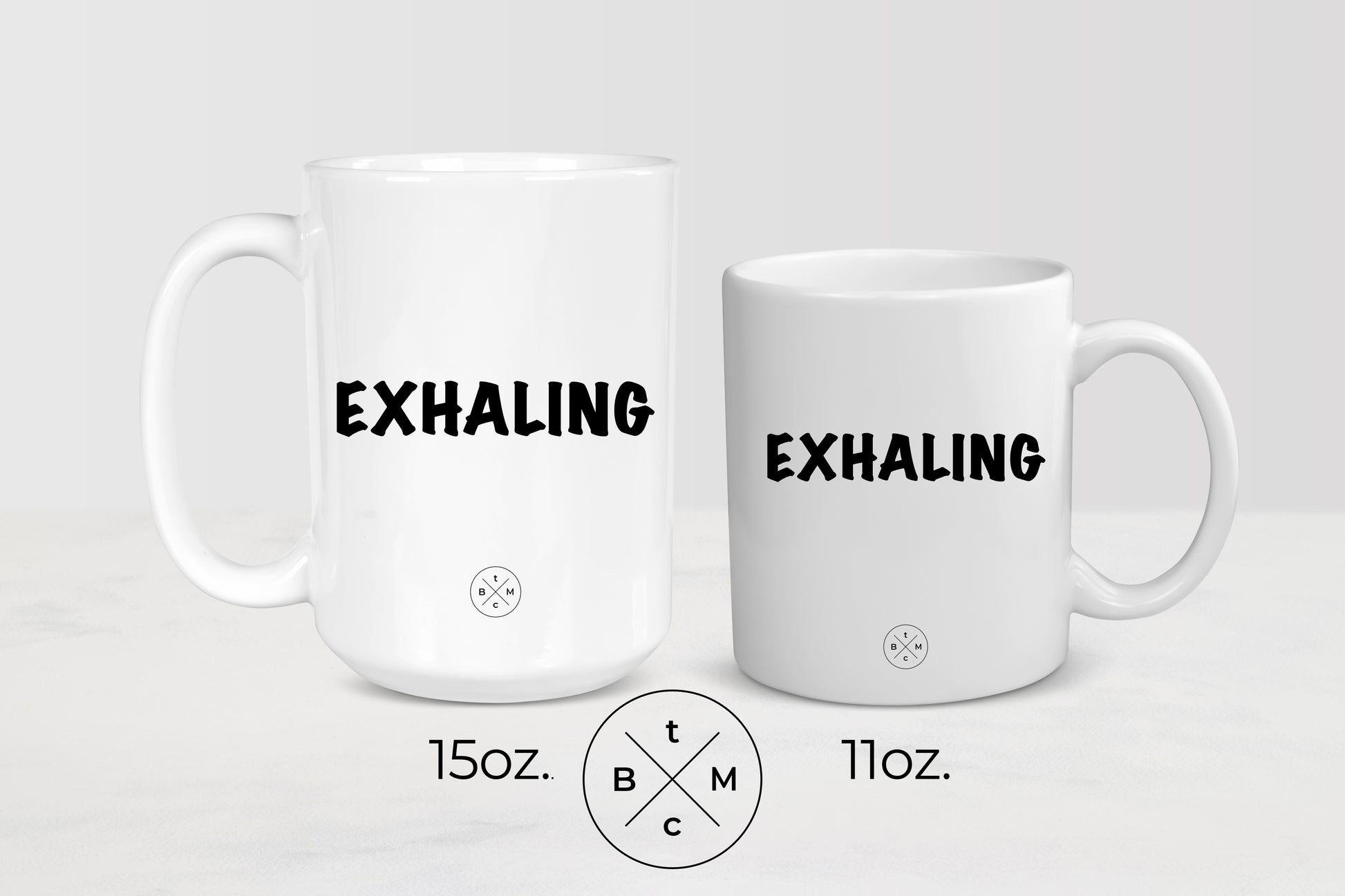 White 11 ounce and 15 ounce ceramic mugs with black text exhaling
