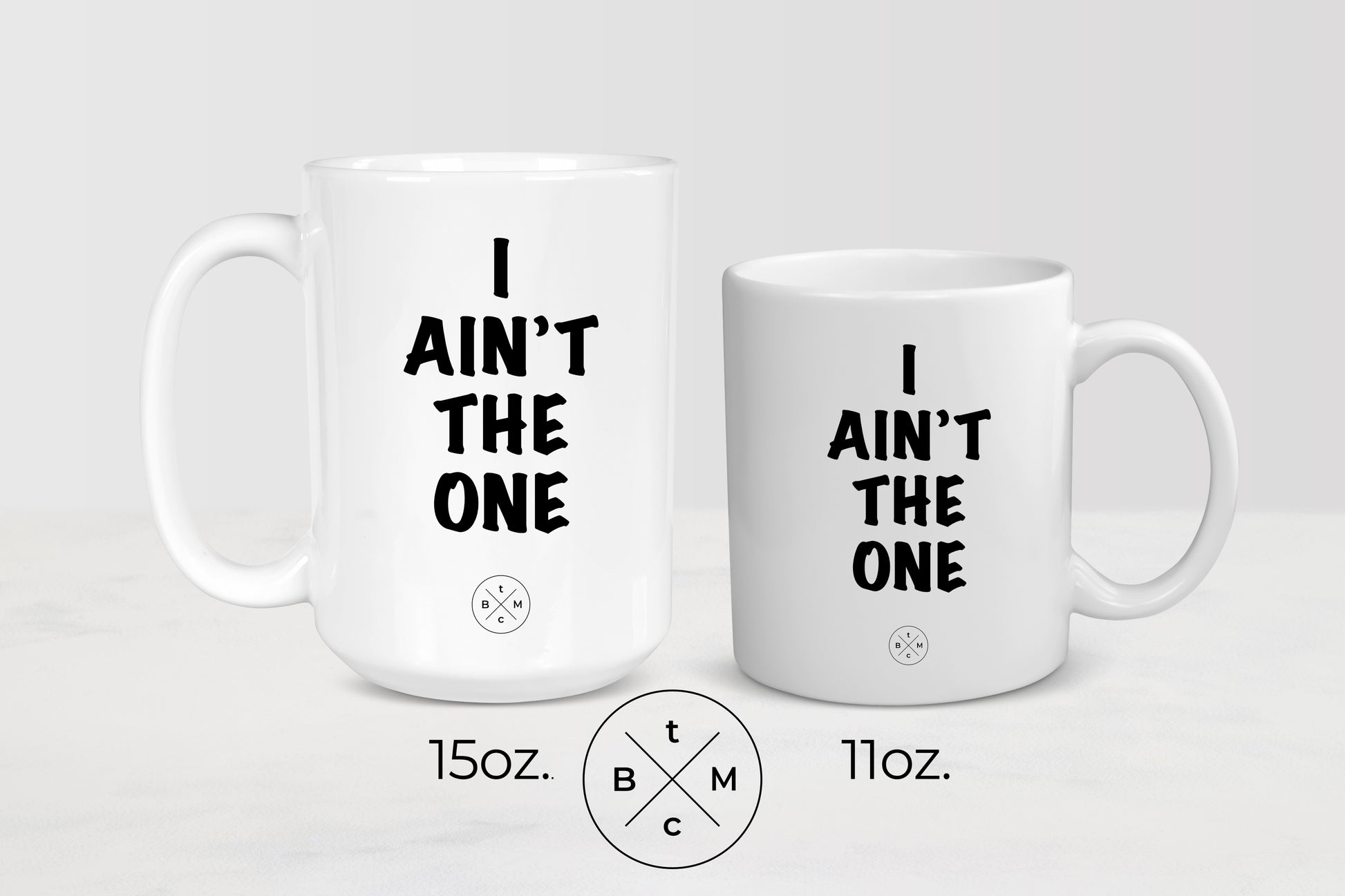 11 ounce and 15 ounce  white ceramic mugs with black text I ain’t the one